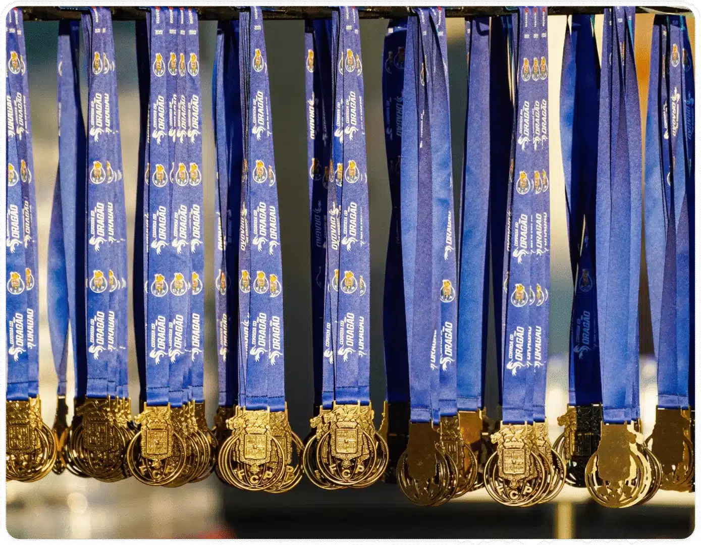 Várias medalhas da Corrida do Dragão penduradas. Cordão azul e medalha dourada.